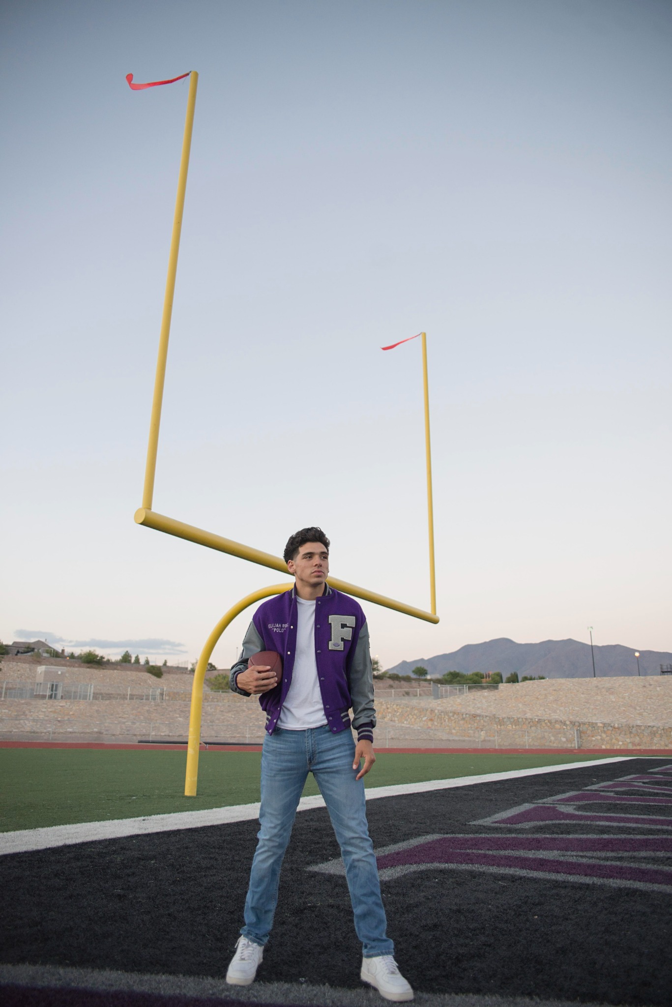 High school senior in his letterman jacket on the football field
