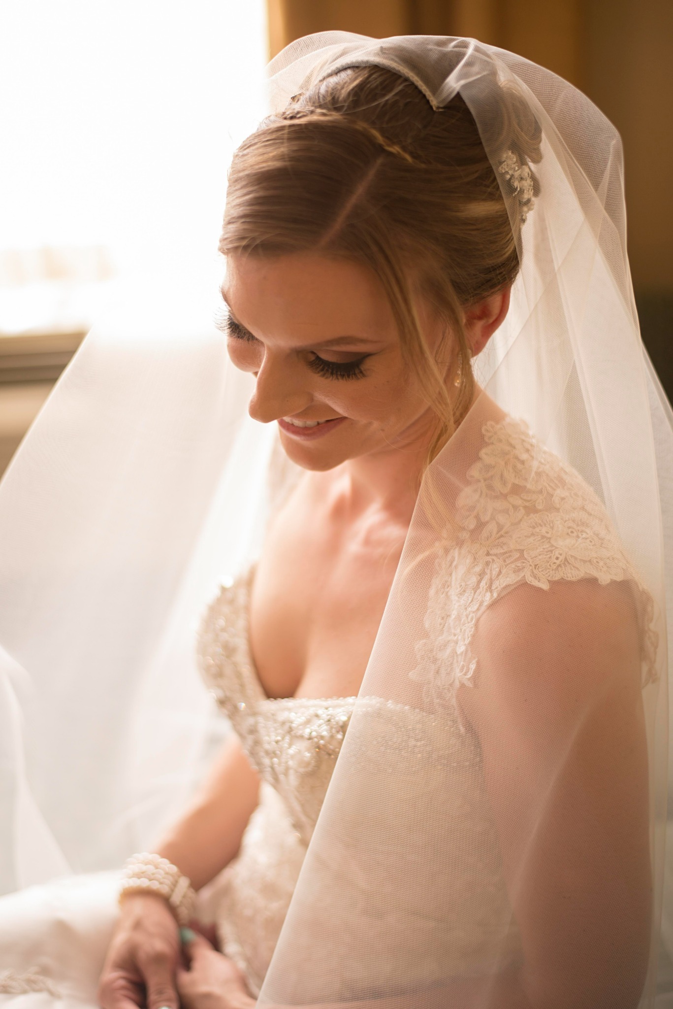 Bride smiling beneath her veil while getting ready