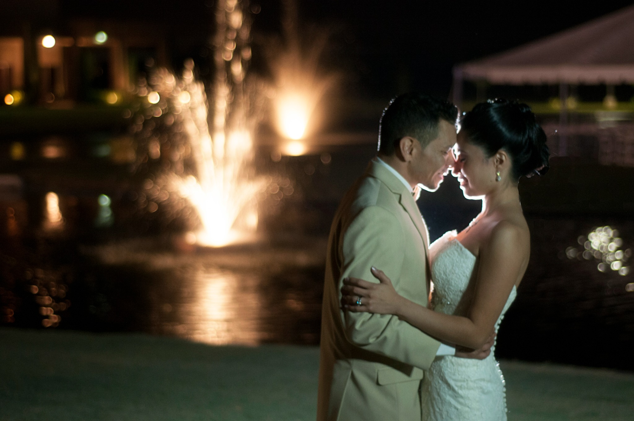 Newlyweds photographed at night beside a glowing fountain